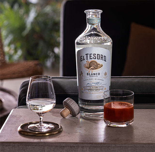 A bottle of El Tesoro Blanco Tequila poured neat into a snifter glass.