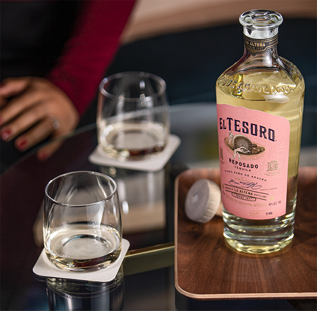 A bottle of El Tesoro Reposado Tequila poured neat into rocks glasses.