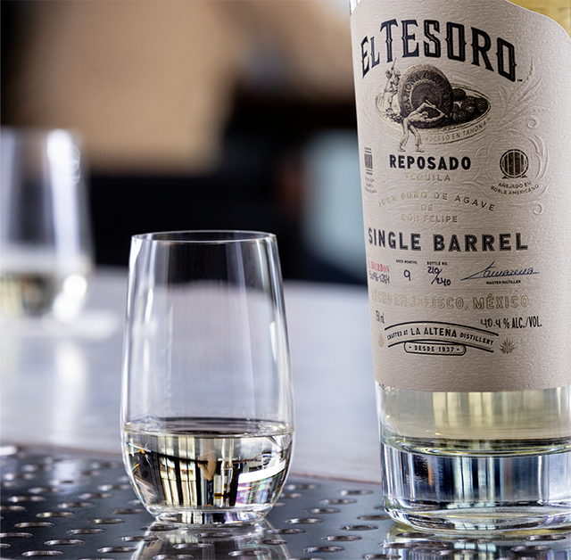 A bottle of El Tesoro Single Barrel Tequila poured neat into a snifter glass.